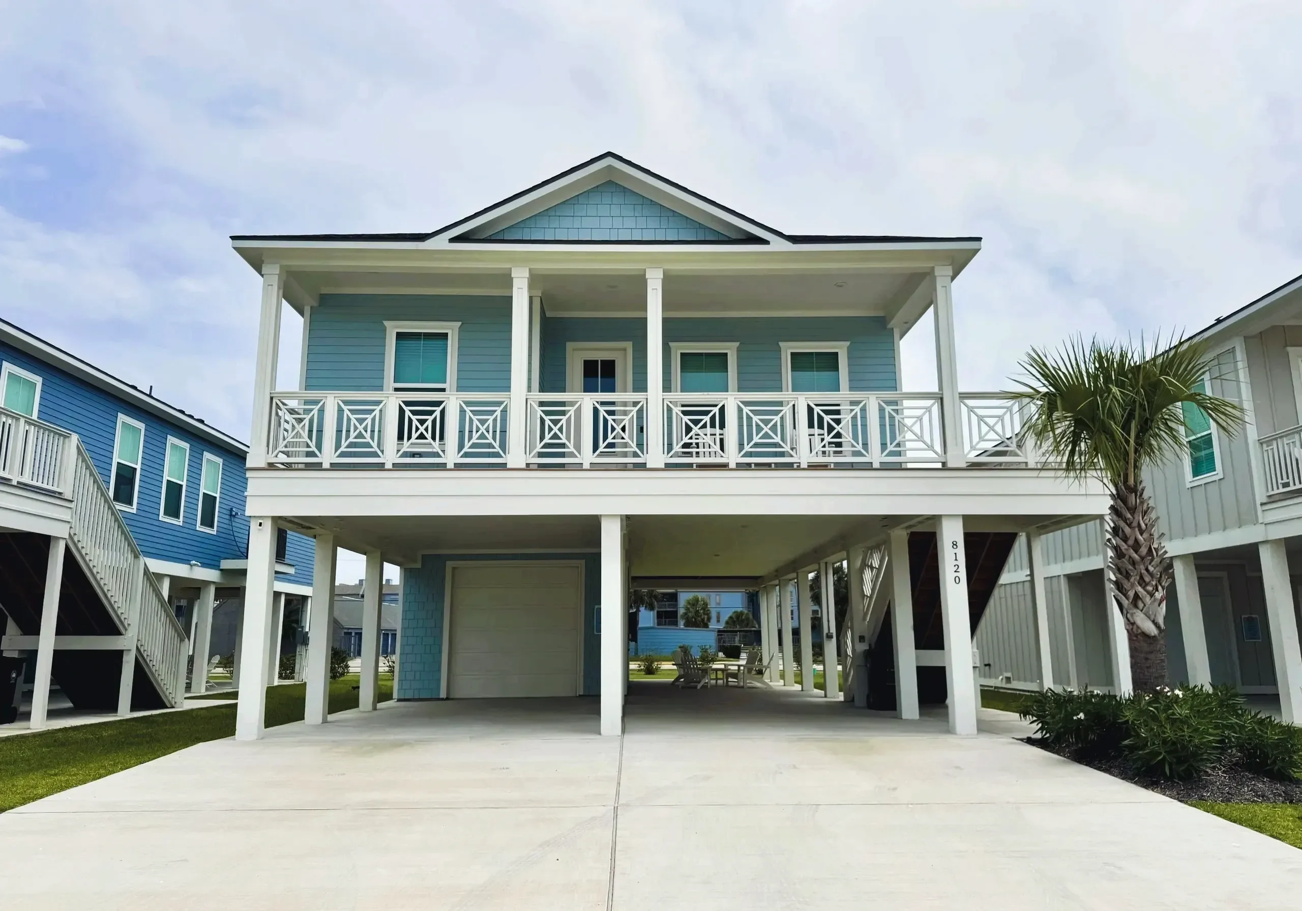 Elevated blue beach house with palm tree.